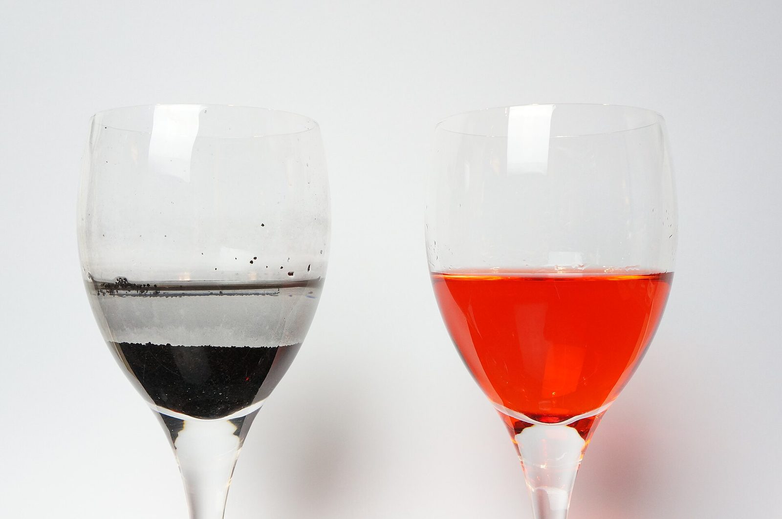 Two glasses: granular activated carbon has cleared red dye from the water on the left